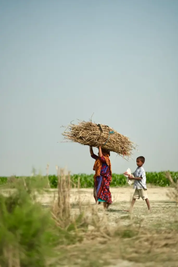 Eine Frau trägt ein Bündel, ein Kind geht neben ihr · Bangladesch